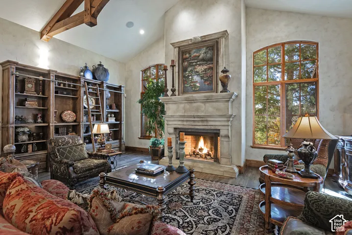 Vaulted ceiling with exposed wood beam, stone-surround fireplace, built-in shelving with rolling ladder, and large arched windows with wood frames