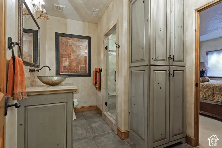 Vessel sink with wall-mounted faucet, custom vanity, tiled flooring, glass-enclosed shower, and built-in cabinetry