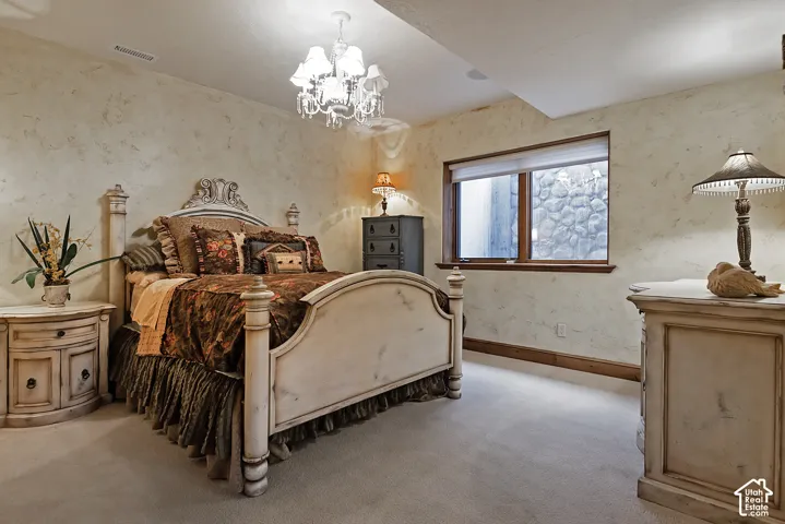 Textured wall finish, ceiling-mounted chandelier, carpeted flooring, wood-framed window, stone-lined exterior window well