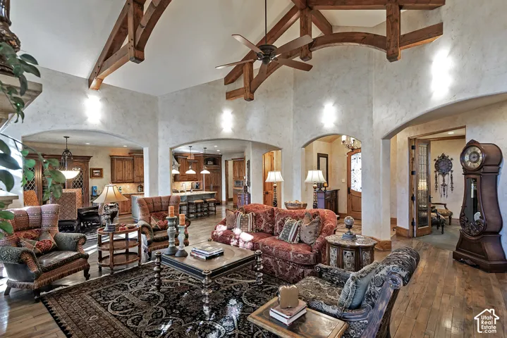 Vaulted ceiling with exposed wood beams, archway entries, textured wall finishes, recessed lighting, and wood-finish flooring