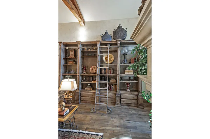 Built-in wood-finish shelving with an attached rolling ladder, exposed ceiling beam, and wood-finish flooring