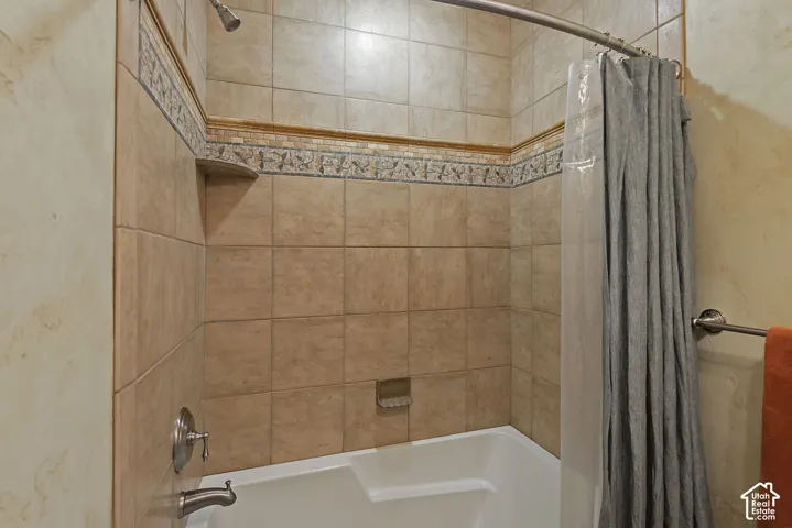 Tiled shower surround with decorative accent band, built-in shelving, and a curved shower rod