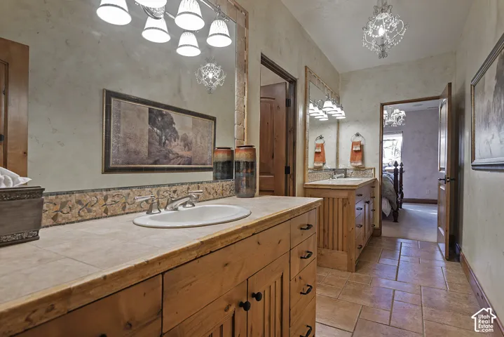 Dual sink vanity featuring wood-finish cabinetry, tile countertops, and a full-width mirror
