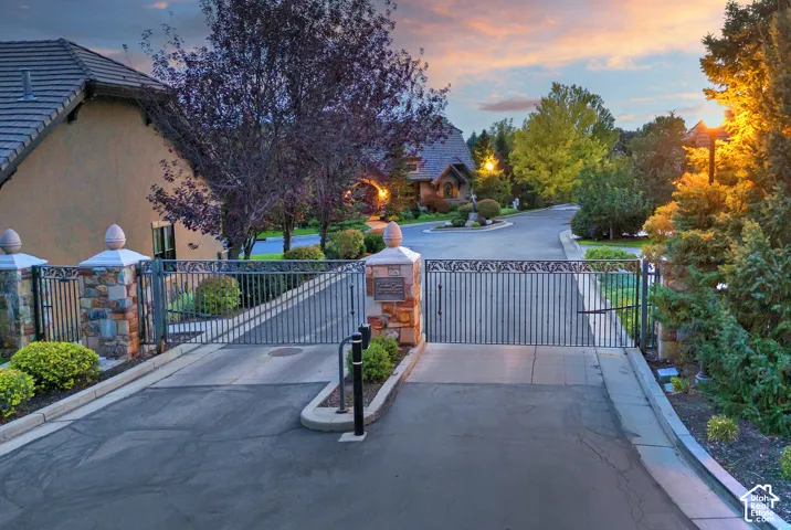 Gated entry featuring stone pillars, decorative wrought iron, and lush landscaping