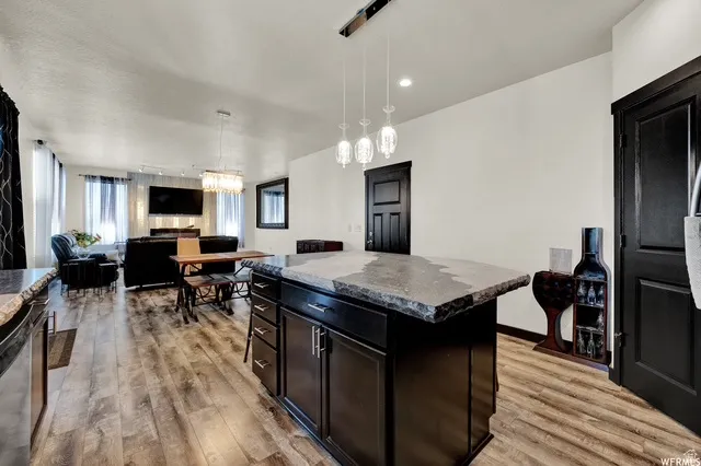 Kitchen island with dark cabinetry and a stone-finish countertop, wood-finish flooring, recessed lighting, and pendant lighting fixtures