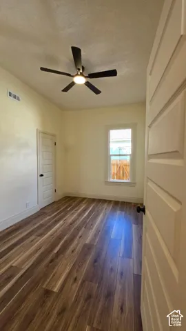 Wood-finish flooring, ceiling fan with integrated lighting, white trim, and a paneled door