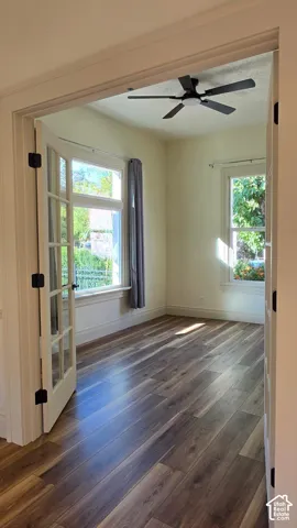 Wood-finish flooring, French doors, multiple windows, and a ceiling fan with integrated lighting