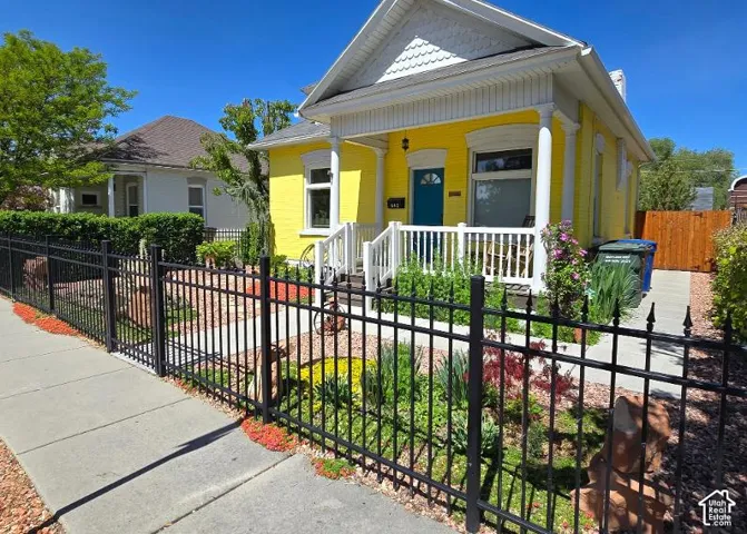 Yellow exterior with white trim, black wrought iron-style fencing, front porch with white railing, blue front door, and mature landscaping
