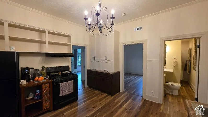 Kitchen featuring wood-finish flooring, dark-toned lower cabinetry with stone-finish countertops, overhead built-in shelving, and a decorative six-arm chandelier