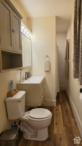 Vanity with integrated sink, wood-finish flooring, built-in wall cabinet, and shower with white tile surround