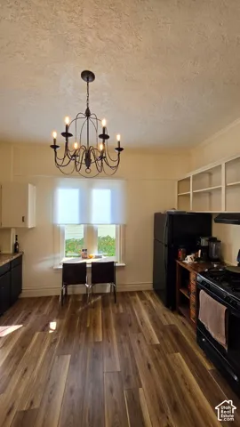 Wood-finish flooring throughout, black appliances, open shelving, and a chandelier with a dark finish