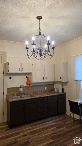 Kitchen featuring two-tone cabinetry, stone-finish countertops, stainless steel double-basin sink with arched faucet, and a decorative six-arm chandelier