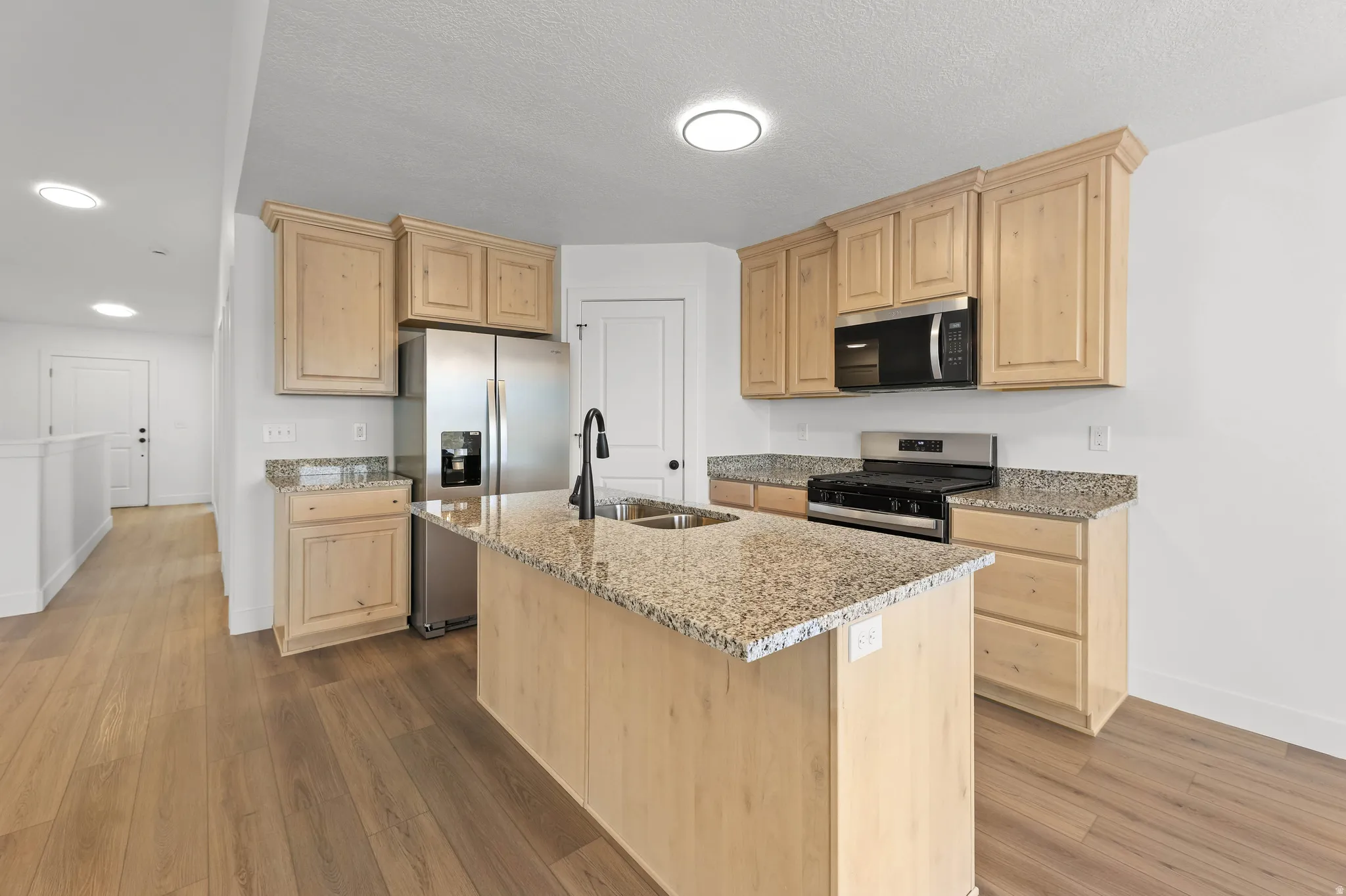 Kitchen featuring an island with a built-in sink, wood-finish cabinetry, stainless steel appliances, and stone countertops