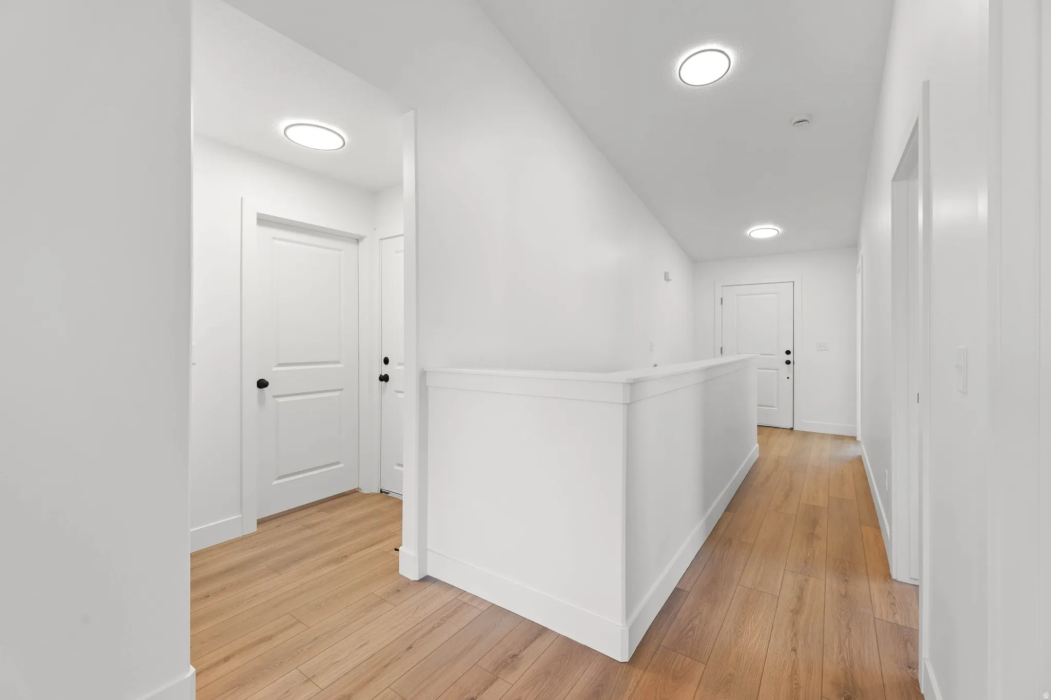 Light wood-finish flooring, recessed ceiling lighting, and white paneled doors with black hardware