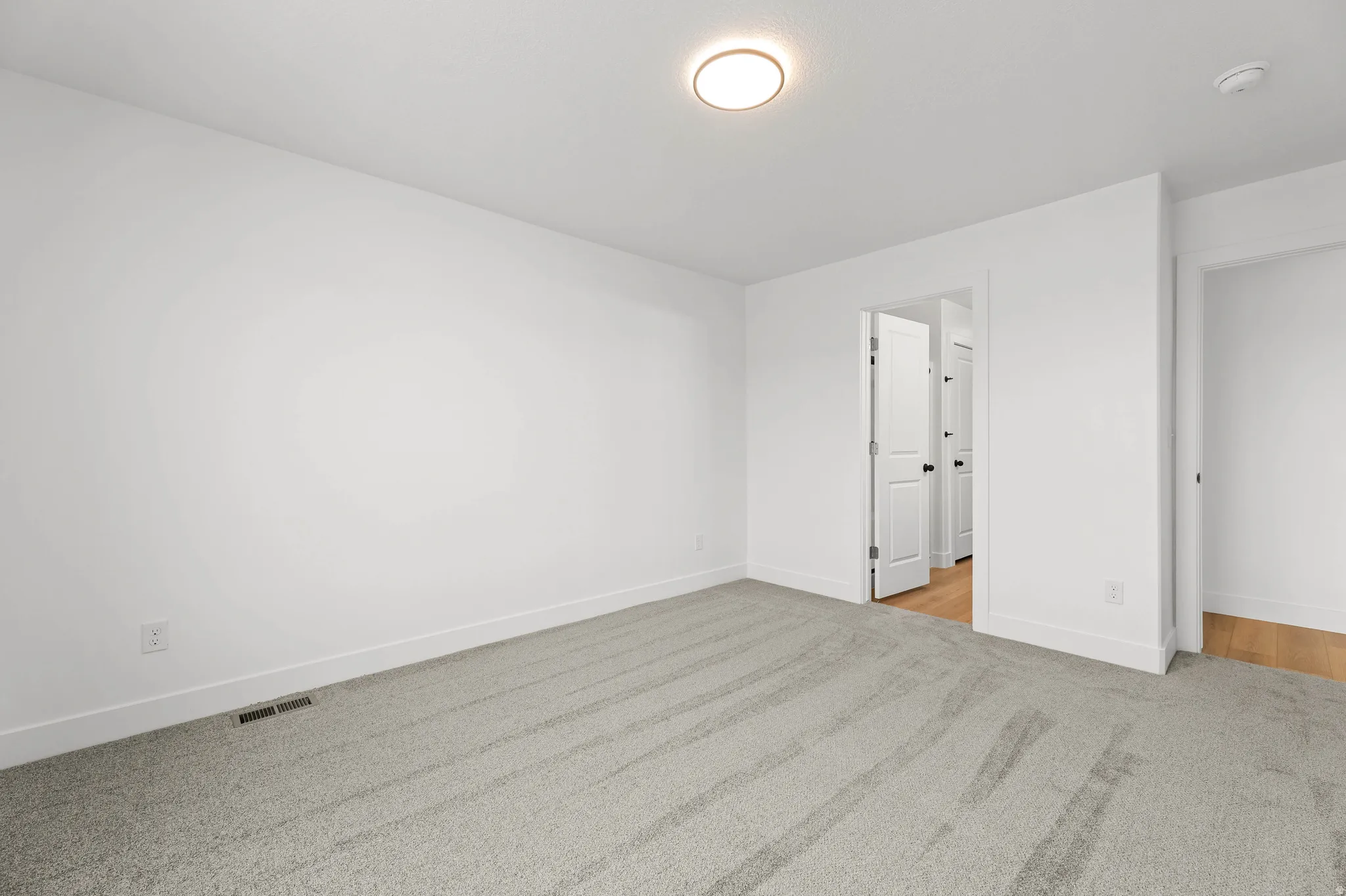 Neutral paint palette with ceiling-mounted lighting, light-toned carpeting, and white trim
