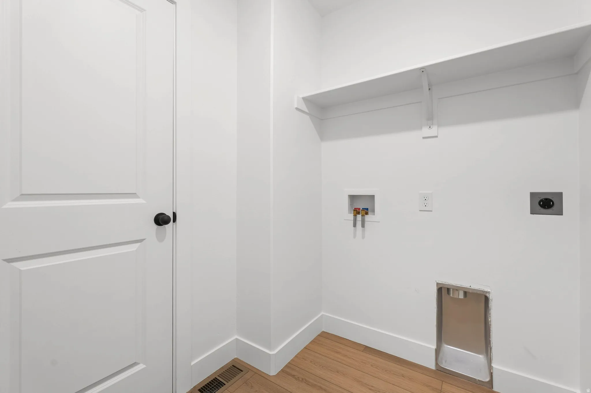 White interior door with a matte black knob, wood-finish flooring, and white wall shelving