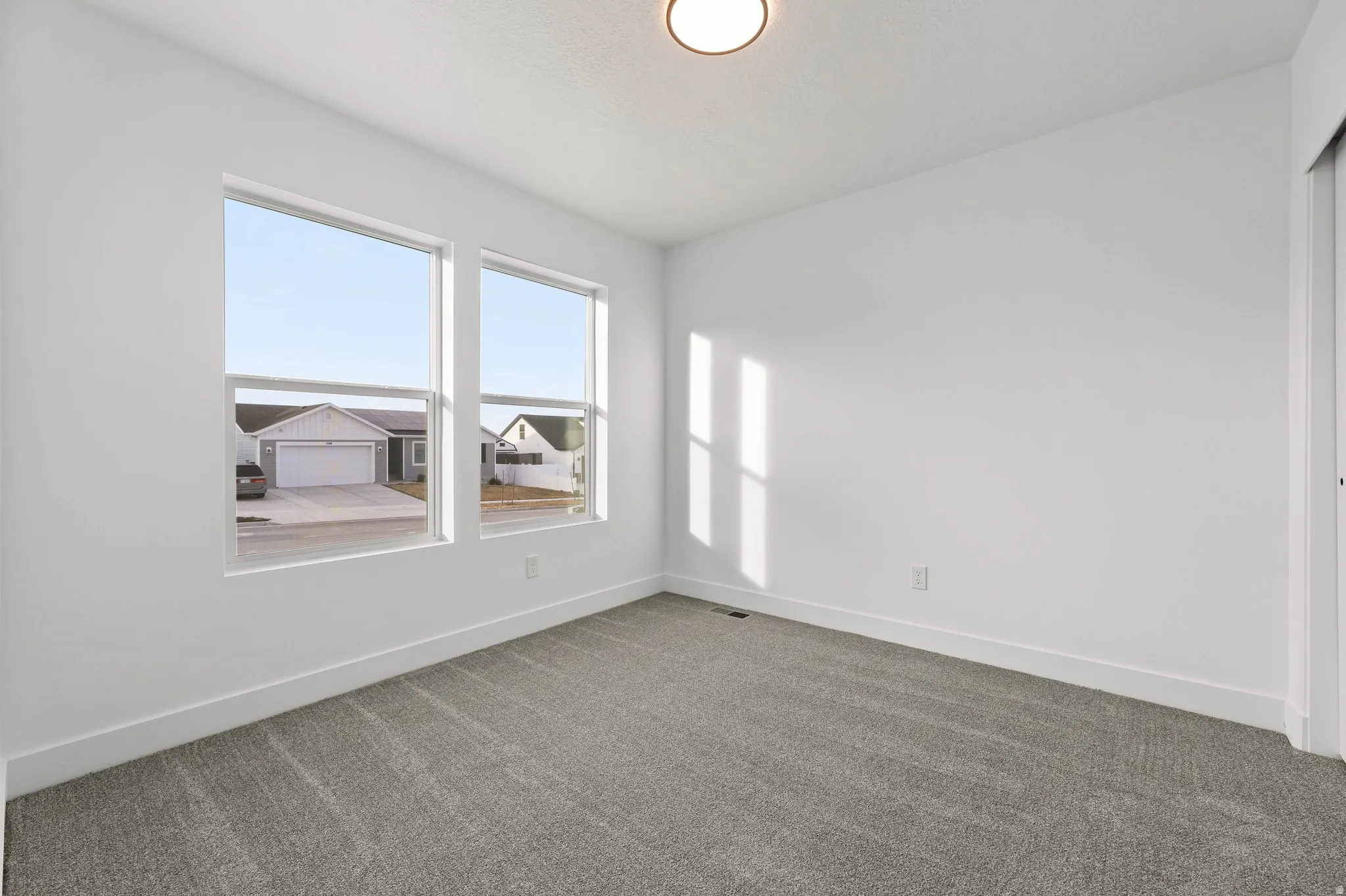 Dual windows, gray carpeting, a flush mount ceiling light, and white walls