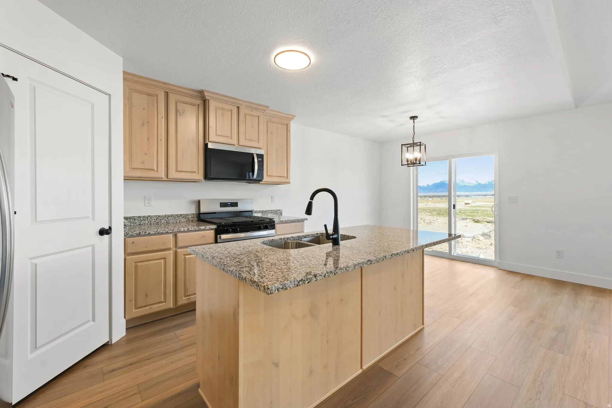 Kitchen featuring wood-finish cabinetry, granite countertops, stainless steel appliances, and a central island with a double basin sink