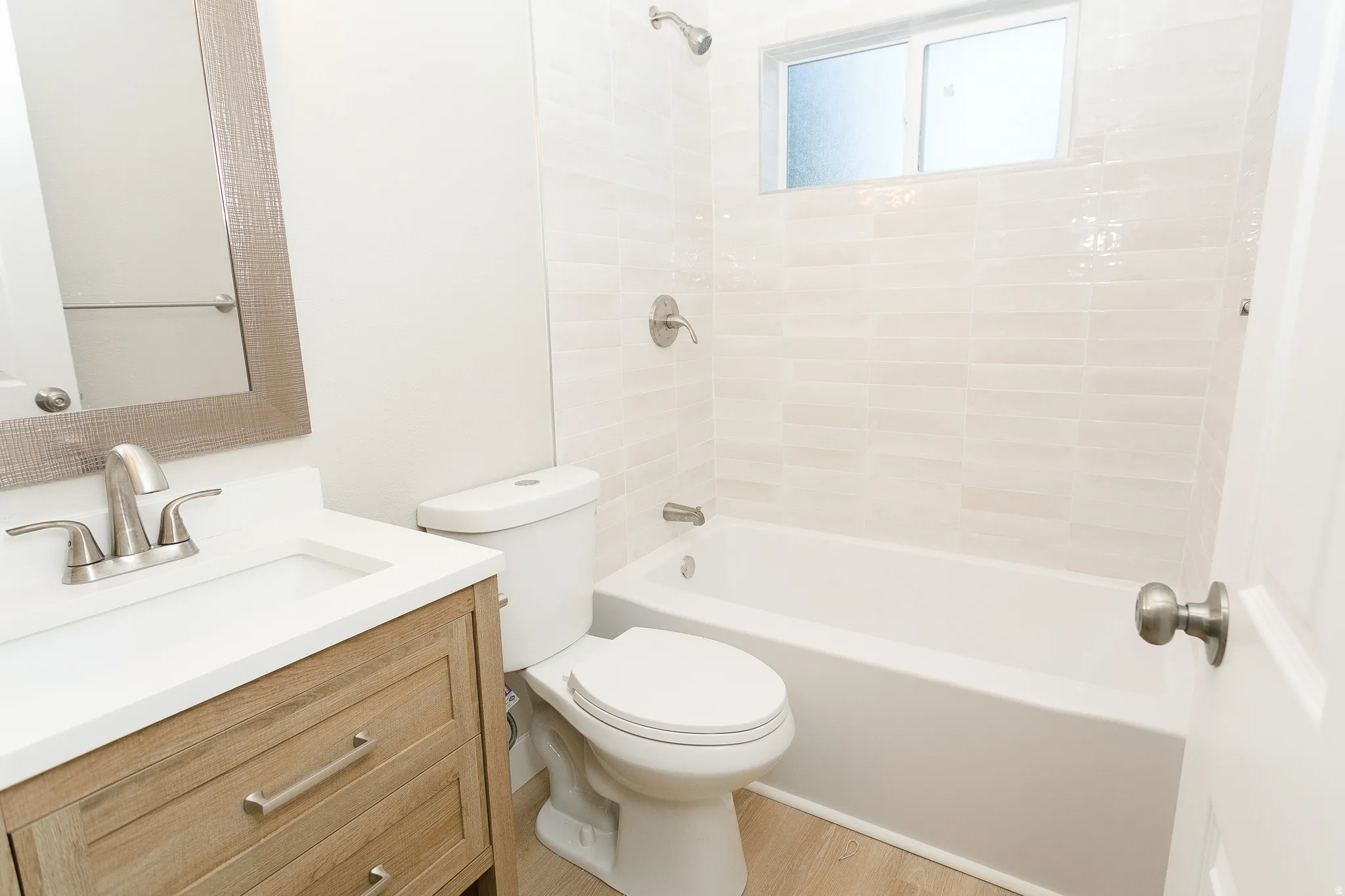 Bathroom featuring a wood-finish vanity with an integrated sink, a framed mirror, a tub with a shower fixture, and a tiled shower surround