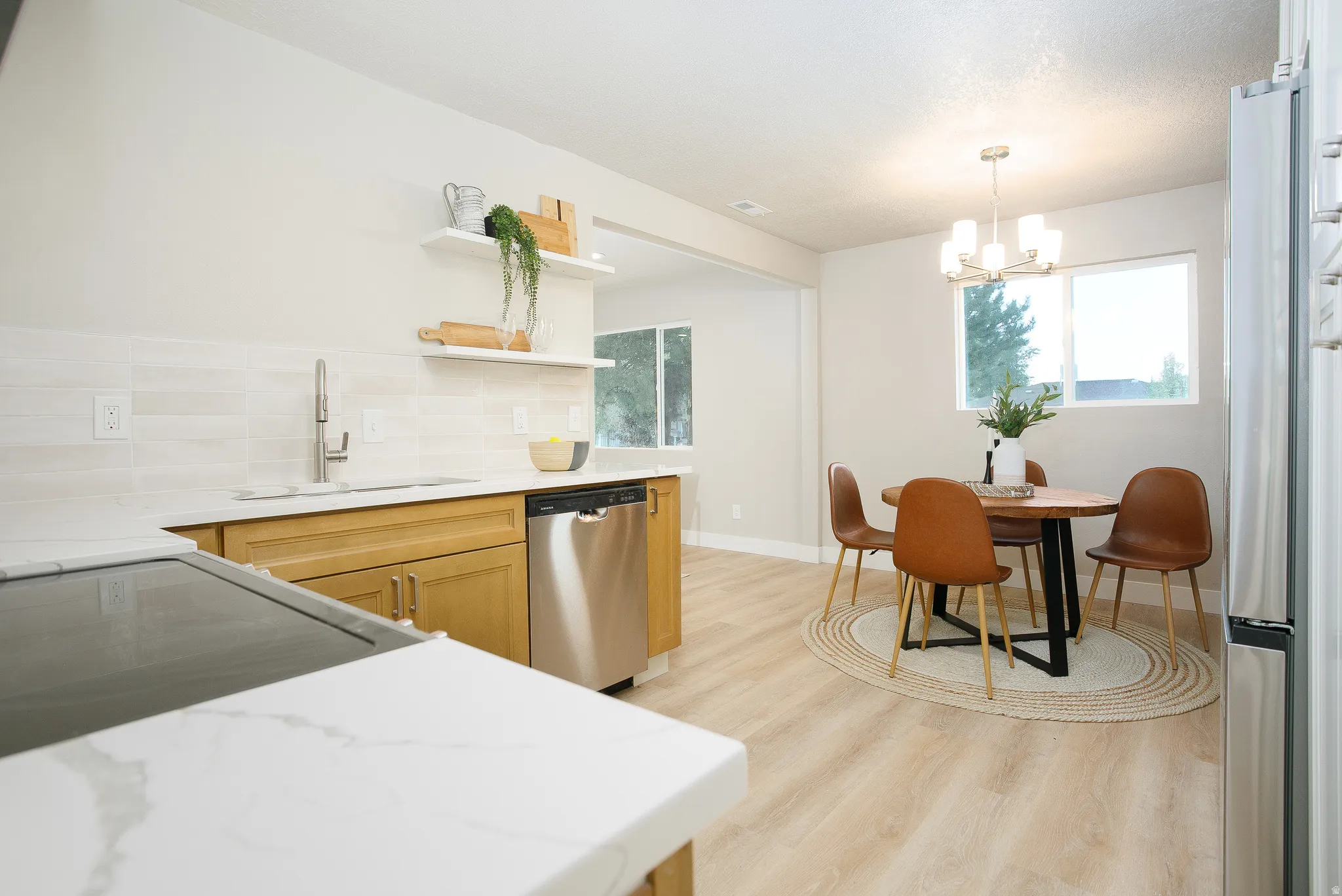 Kitchen featuring white quartz countertops, light wood-finish cabinetry, stainless steel dishwasher, and a white tiled backsplash