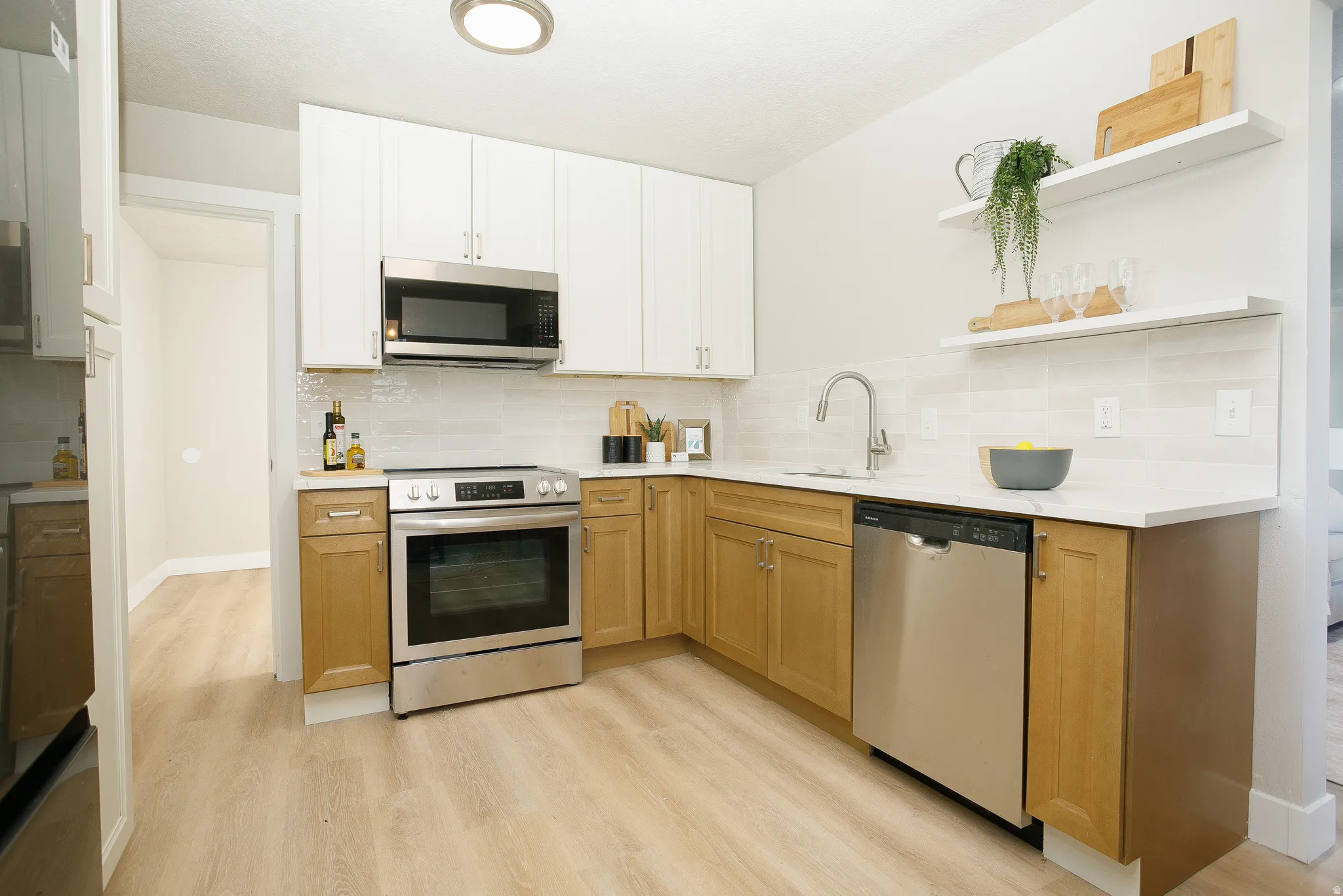 Kitchen featuring two-tone cabinetry, stainless steel appliances, light countertops, a tile backsplash, and wood-finish flooring