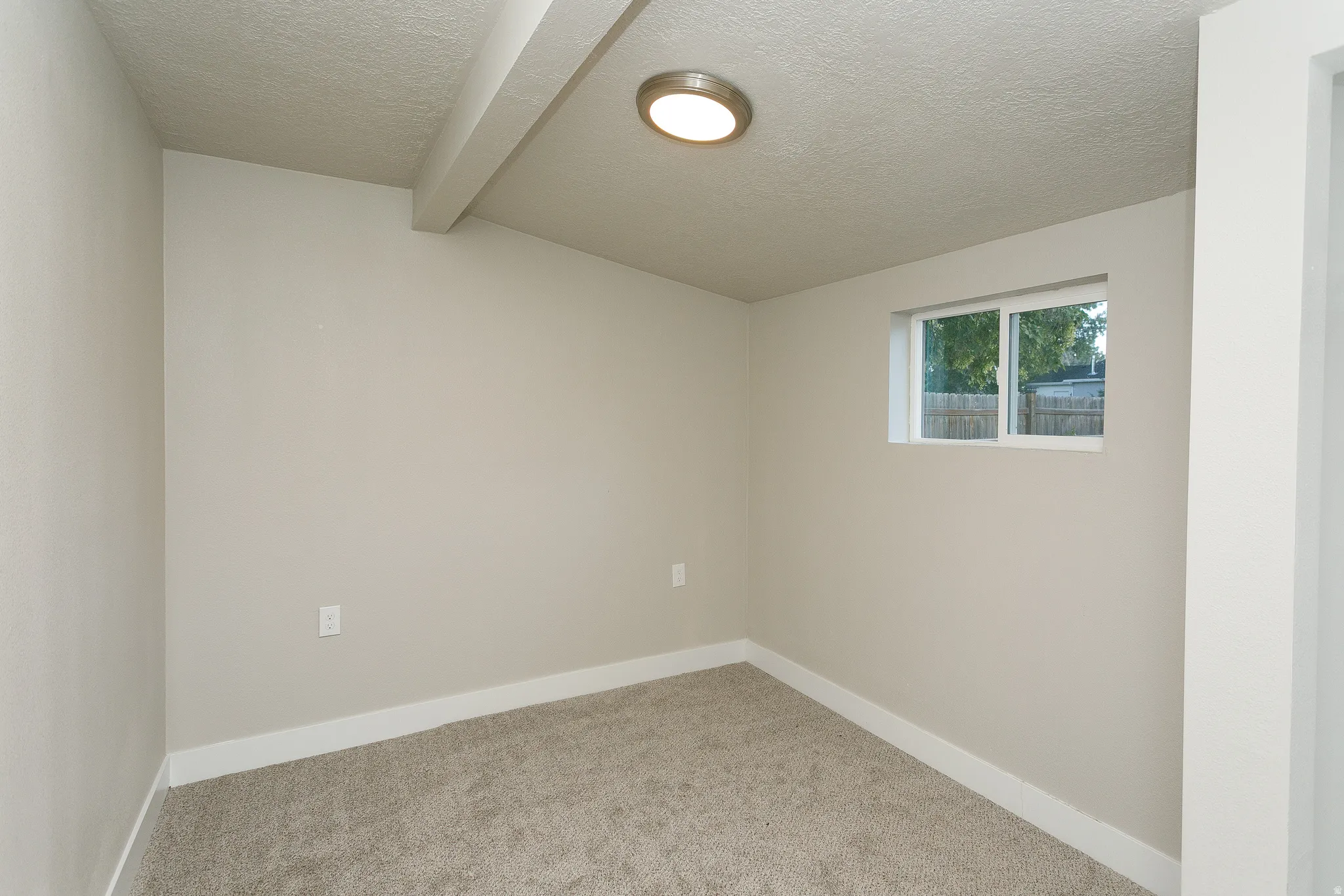 Carpeted flooring, recessed ceiling beam, flush-mount ceiling light, white trim, and a functional window