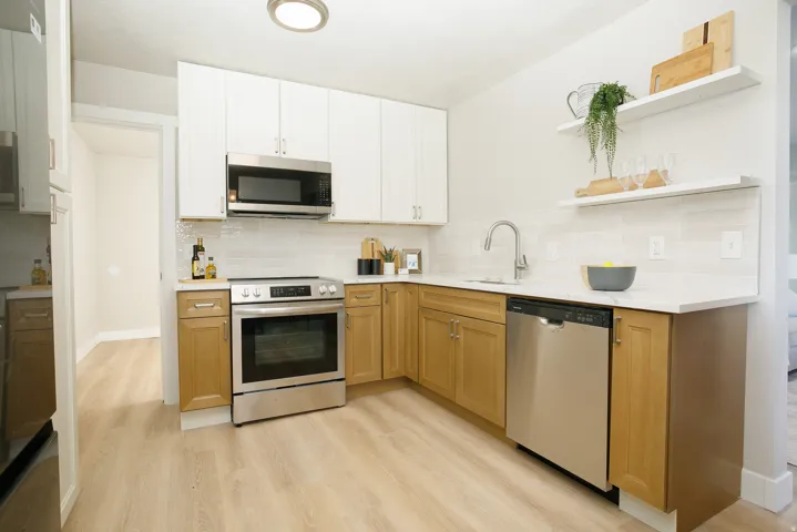 Kitchen featuring two-tone cabinetry, stainless steel appliances, light countertops, a tile backsplash, and wood-finish flooring