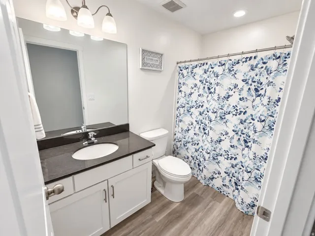White vanity with brushed nickel hardware, dark stone countertop, undermount sink, and wood-finish flooring