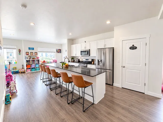 Spacious kitchen featuring an expansive island with seating, white shaker cabinetry, stainless steel appliances, and wood-finish flooring throughout