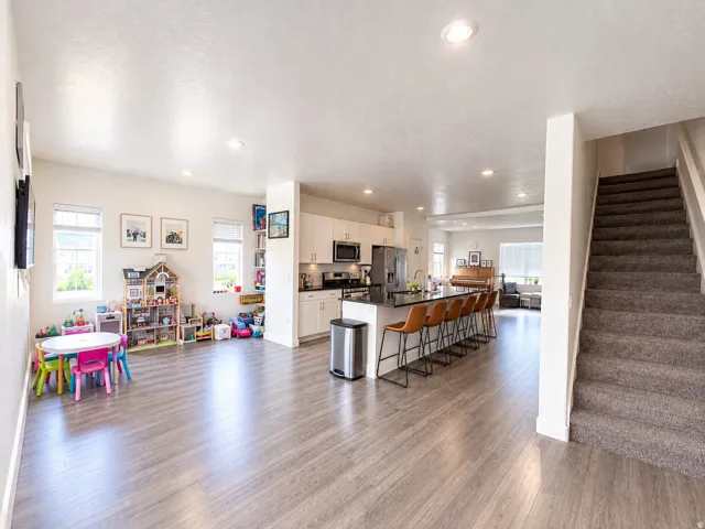 Open-concept living area featuring wood-finish flooring, recessed lighting, and a kitchen with white cabinetry and a dark countertop
