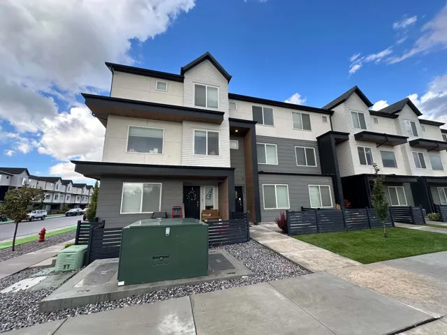 Modern multi-level townhome featuring a mixed material facade, large windows, and a dark-toned privacy fence