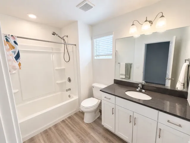 White vanity with shaker-style cabinetry, dark countertop, and integrated sink