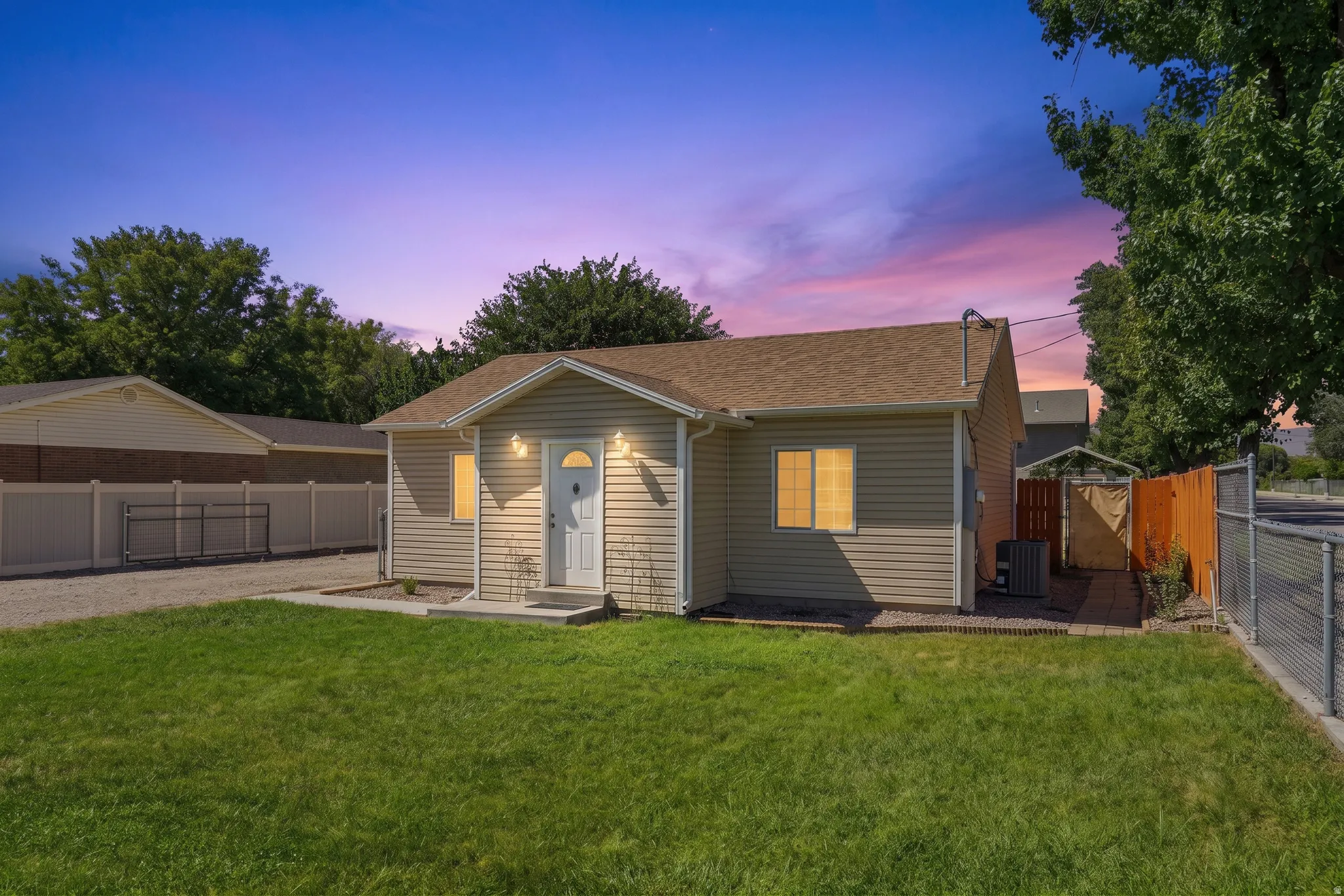 Beige horizontal siding exterior, brown shingle roof, well-maintained lawn, privacy fencing, and chain-link fencing