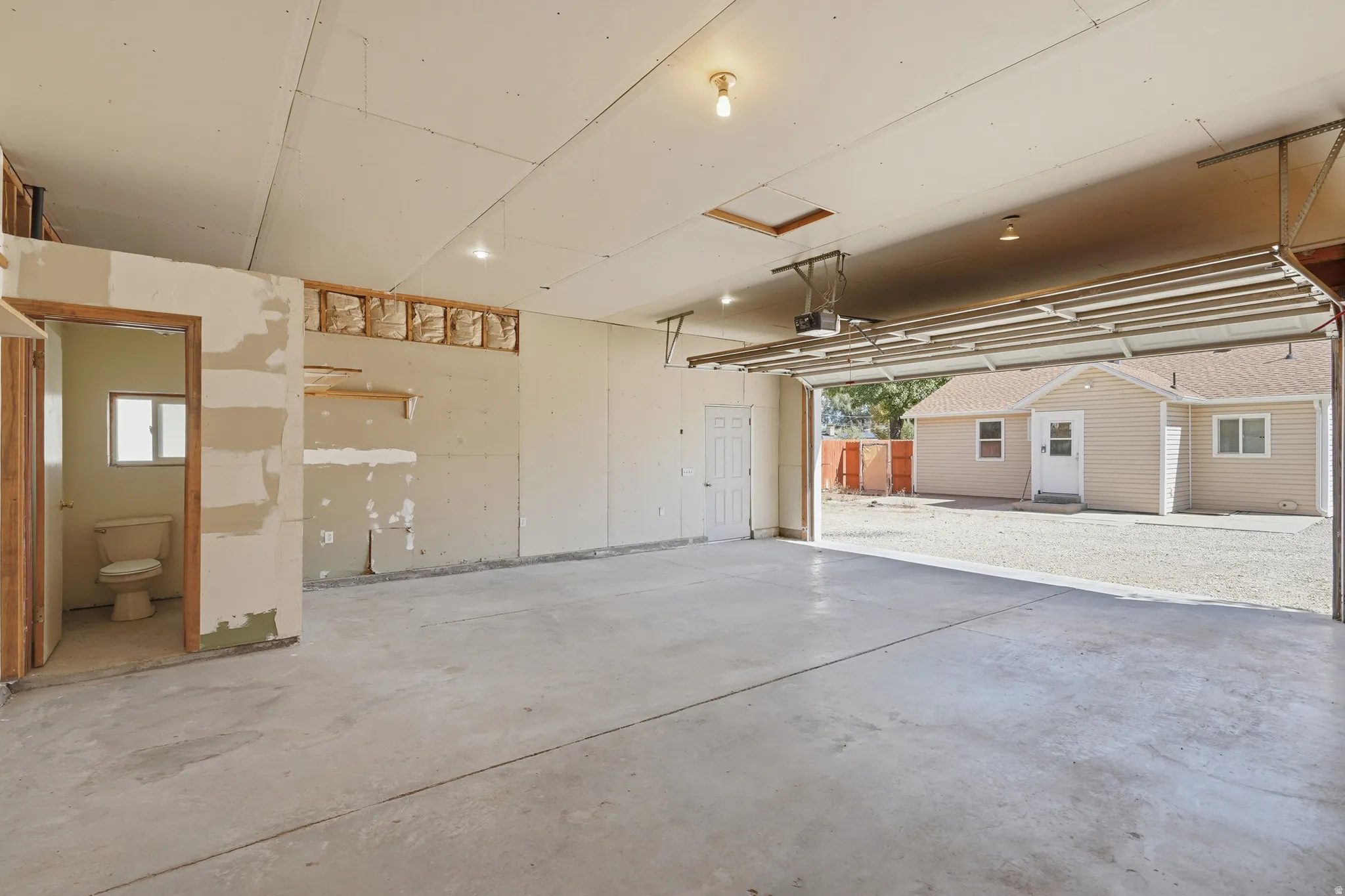 Spacious garage with concrete flooring, automatic garage door opener, and integrated half bathroom