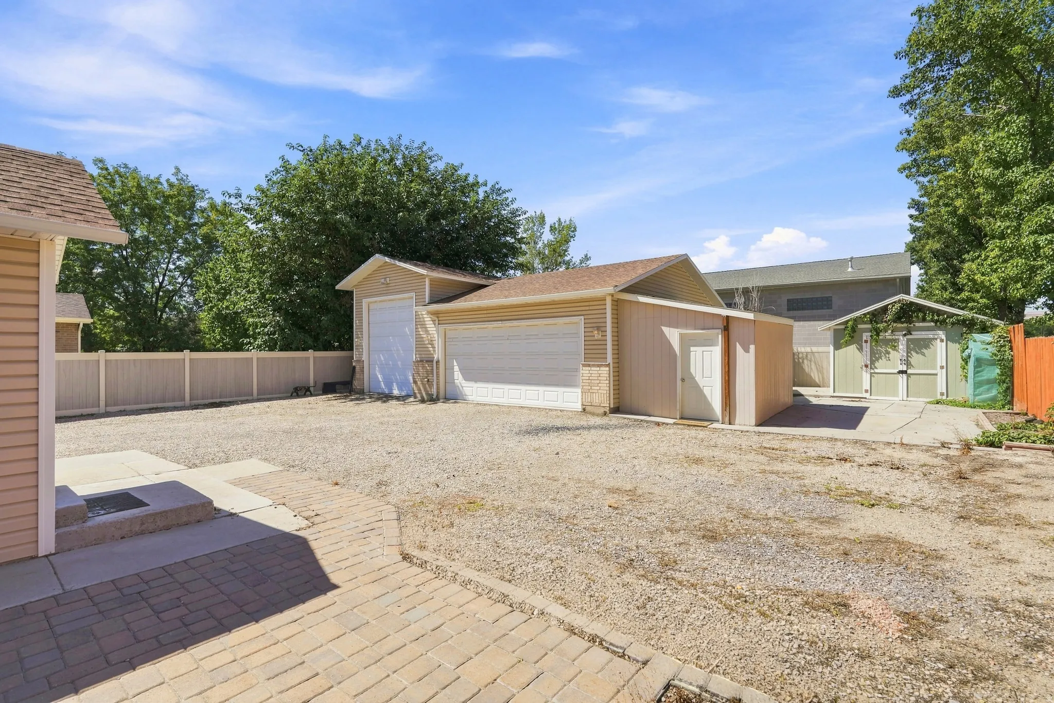 Gravel driveway with brick paver pathway, featuring a detached garage with single door, an additional detached structure, and a separate shed with double doors