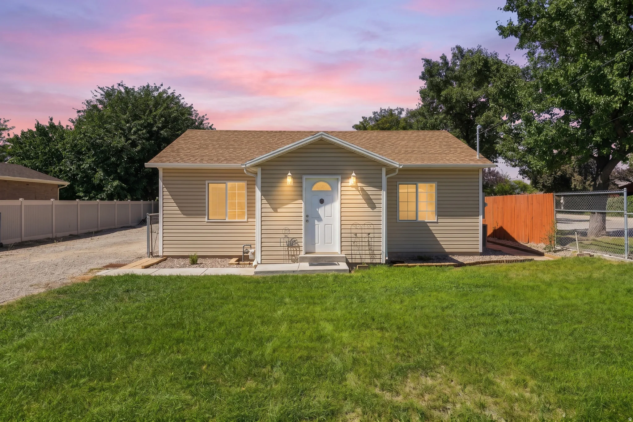 Gabled roofline, light-colored siding, front entry, front yard, and gravel driveway