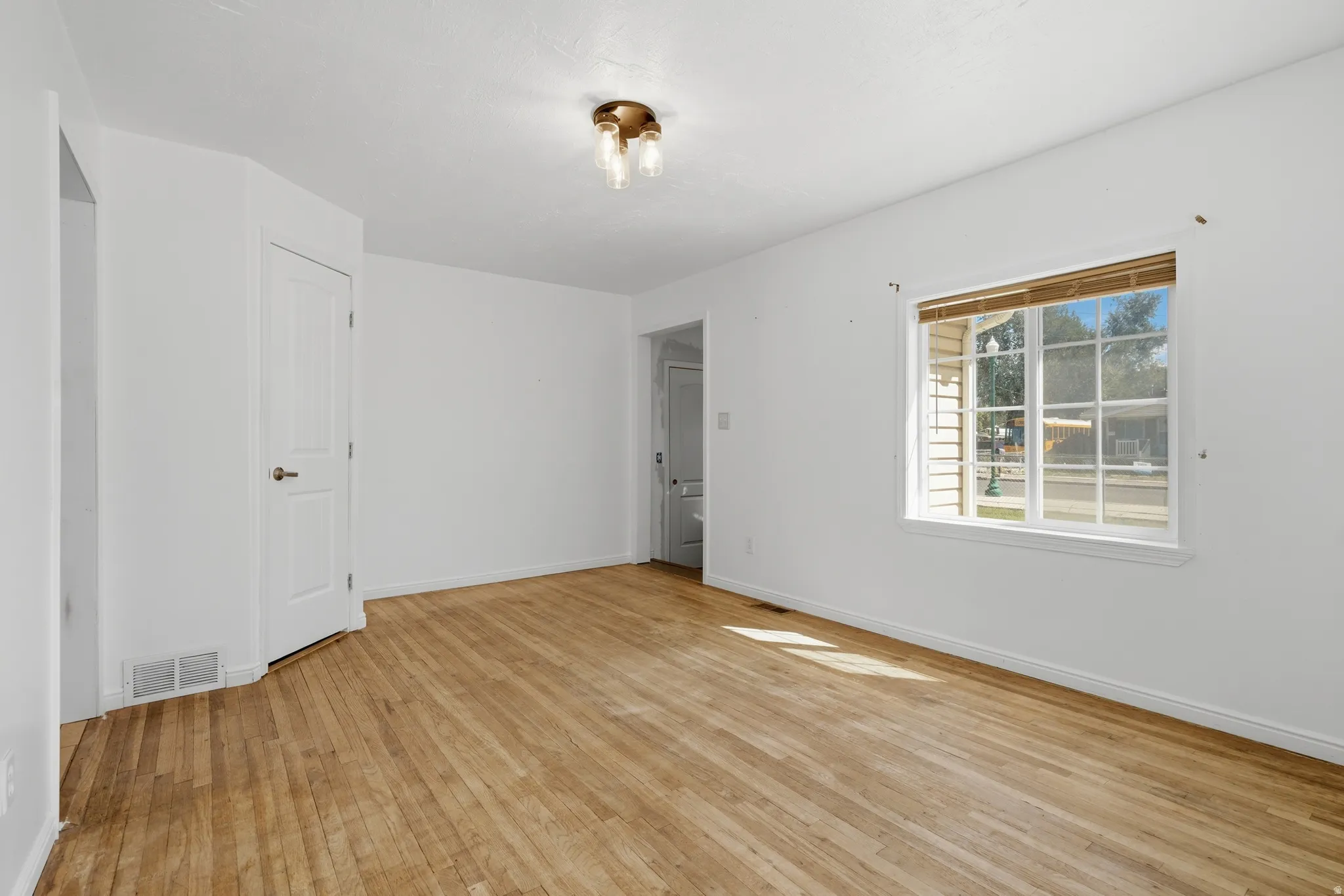 Hardwood flooring, white walls, white window frame, white door, and a bronze-finish ceiling fixture