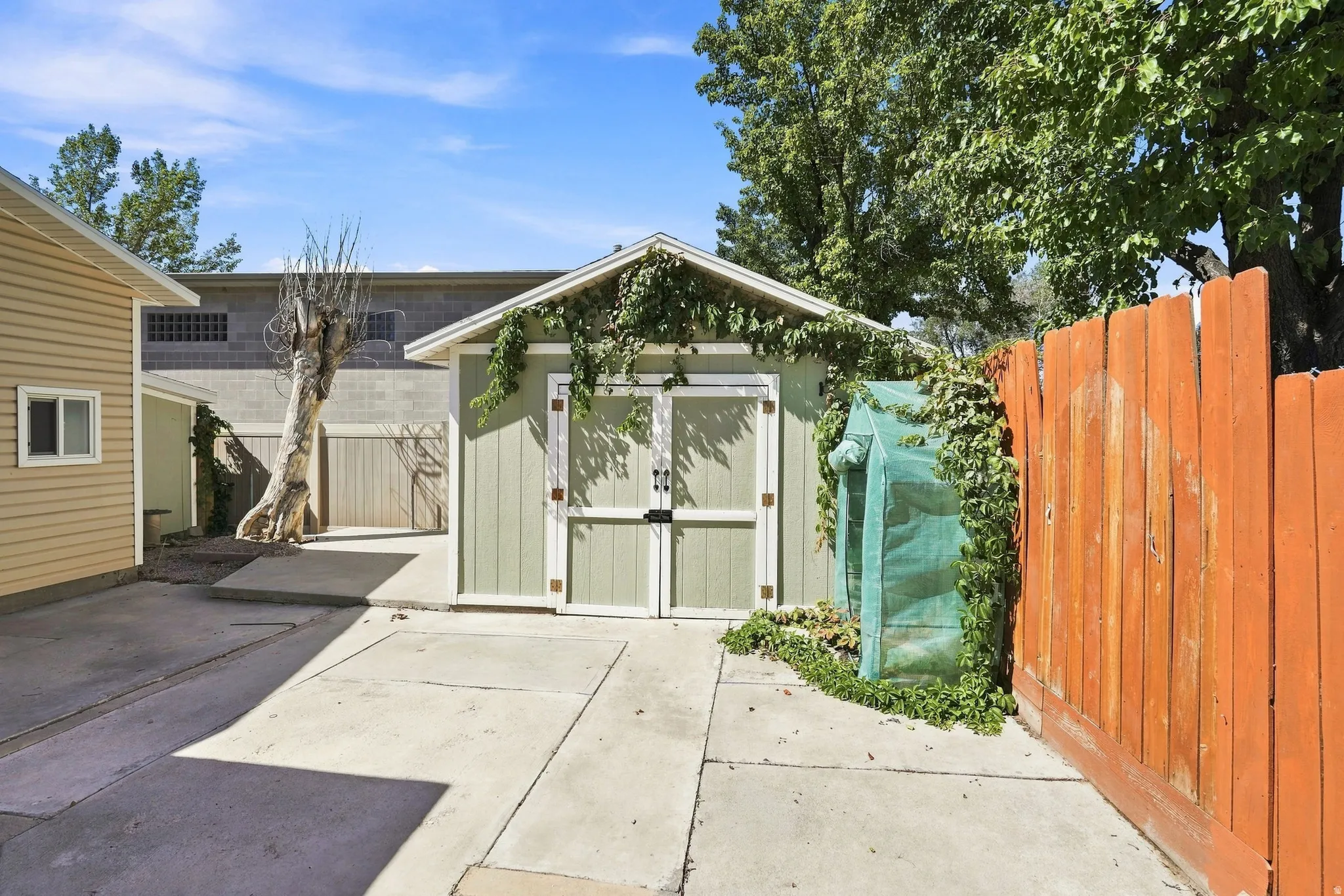 Storage shed with double doors, concrete paving, and an orange wooden privacy fence