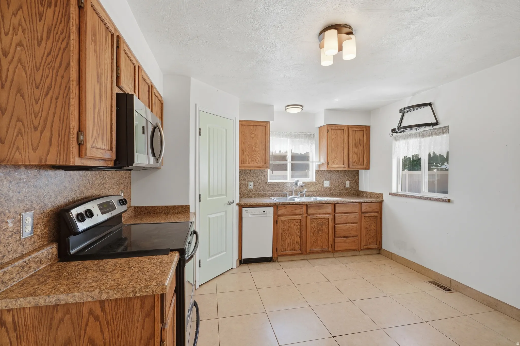 Kitchen featuring wood cabinetry, solid surface countertops with backsplash, stainless steel microwave, electric range, and tile flooring