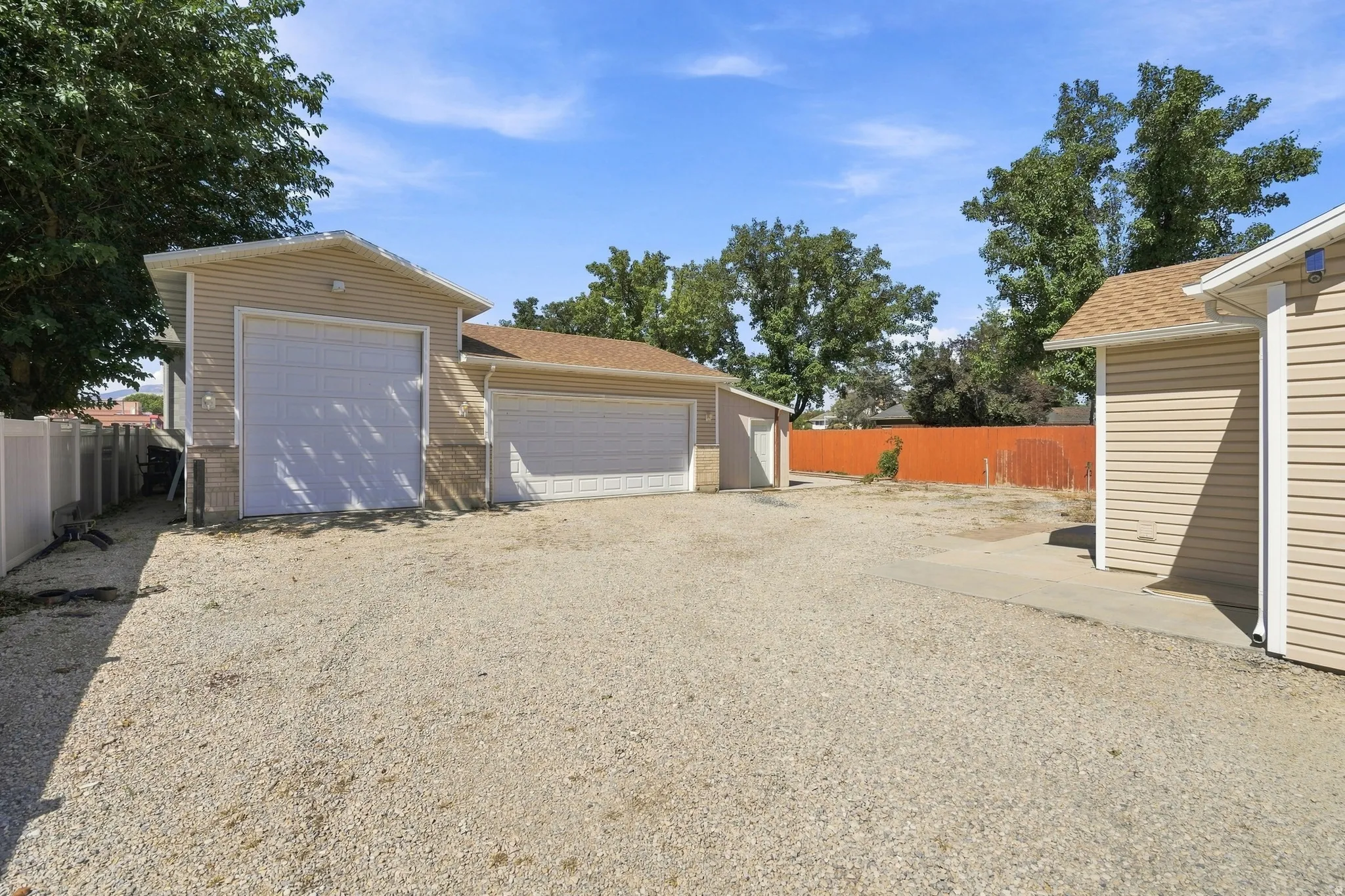 Detached garage structure with a large overhead door, an additional attached garage with a separate overhead door, and a gravel surface
