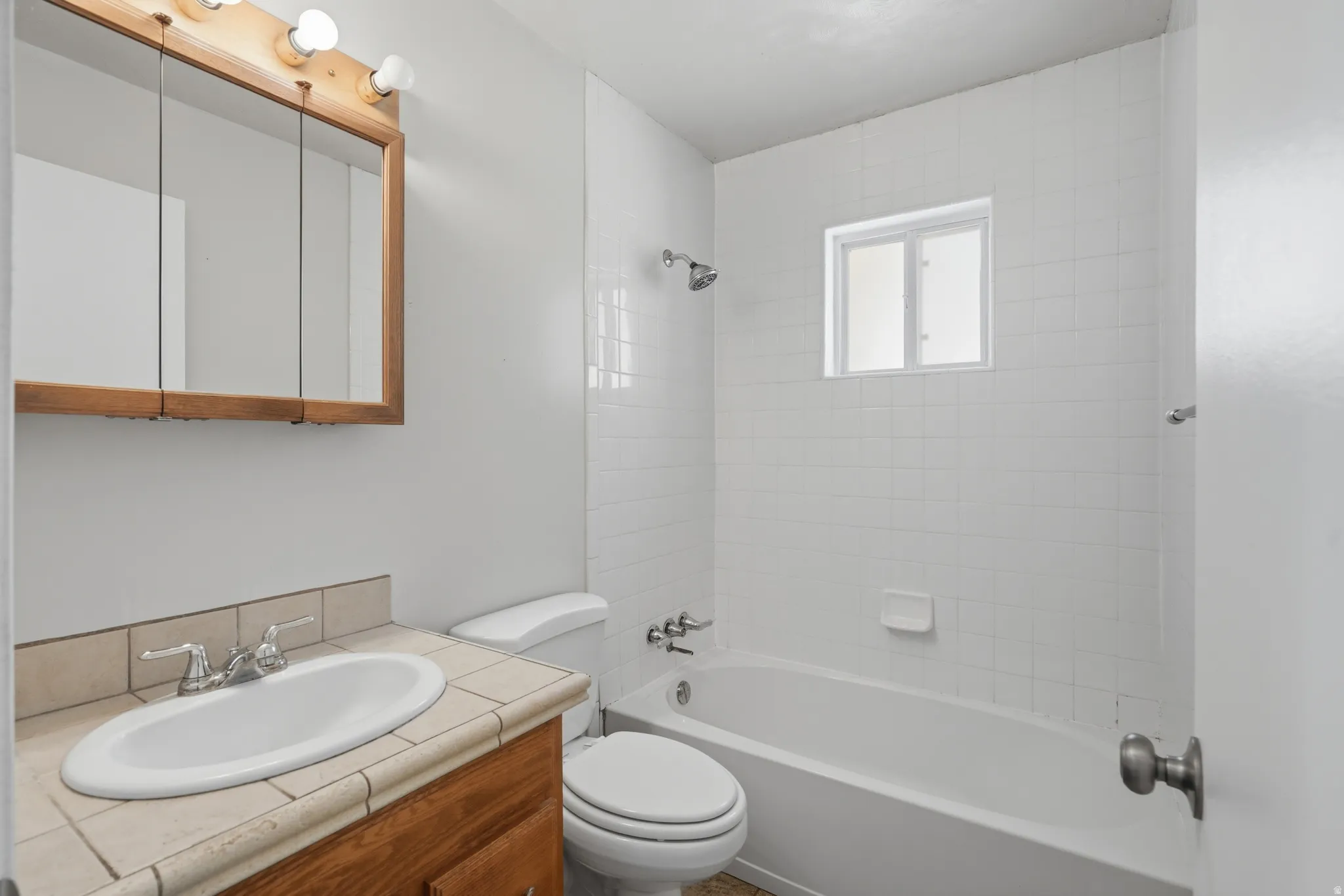 Bathroom featuring a wood-finish vanity with tiled countertop, a white oval sink, and a mirrored medicine cabinet with integrated lighting