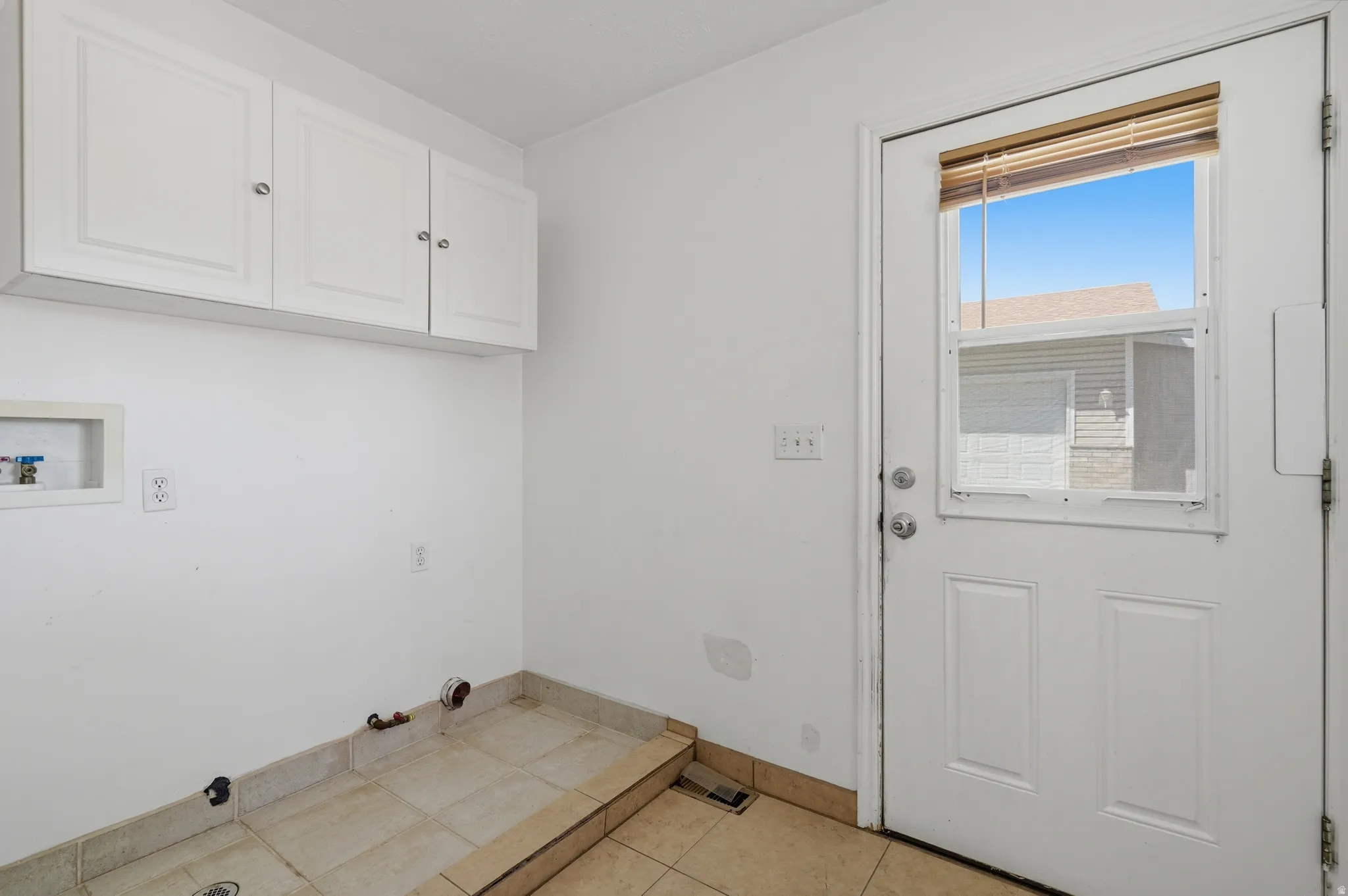 White shaker-style cabinetry with silver hardware, ceramic tile flooring, and a door with an inset window