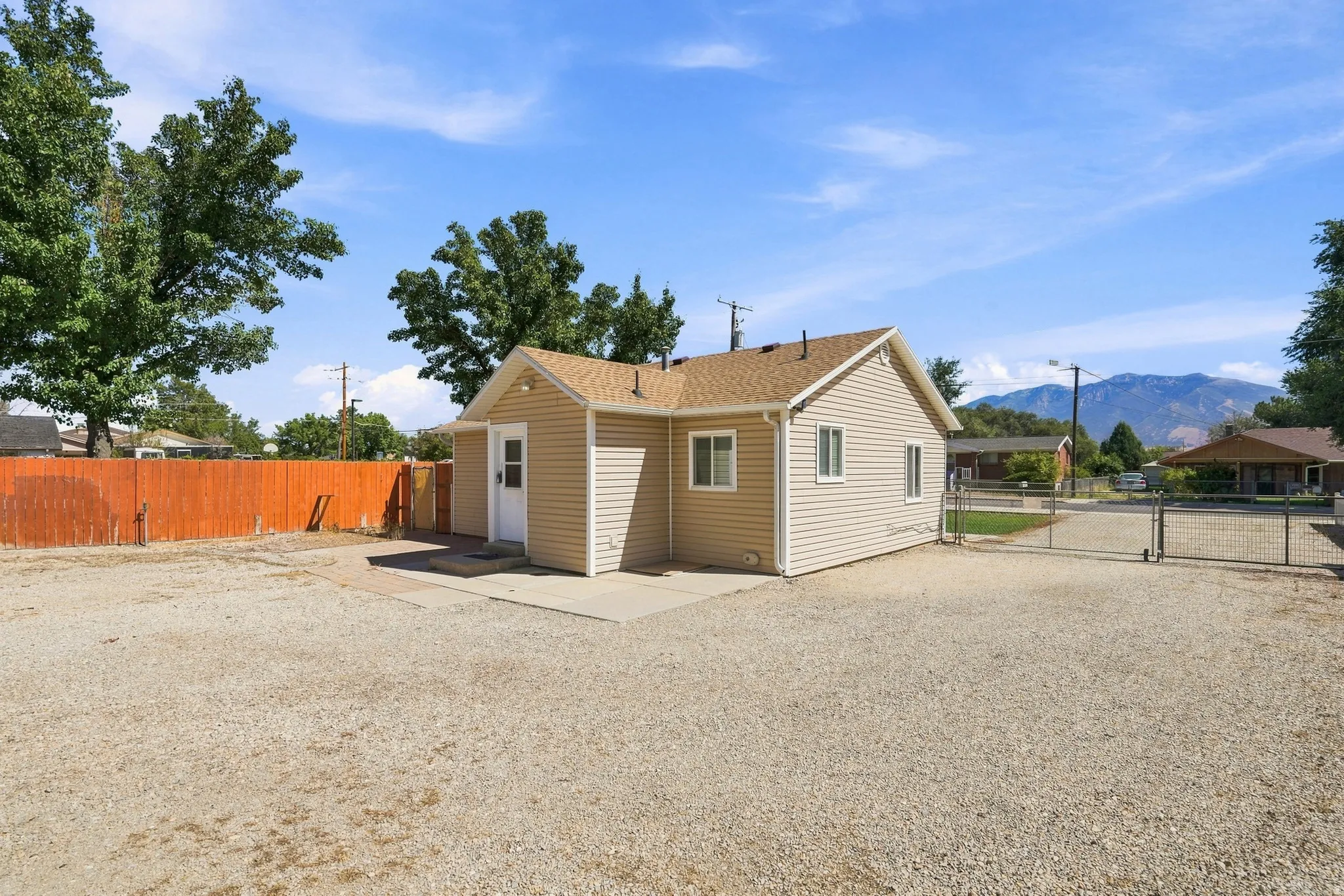 Exterior siding, gravel lot, fenced perimeter, concrete patio, and a metal gate