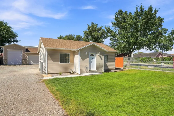 Exterior featuring horizontal siding, a gravel driveway, a detached garage, a chain-link fence, and a mature tree