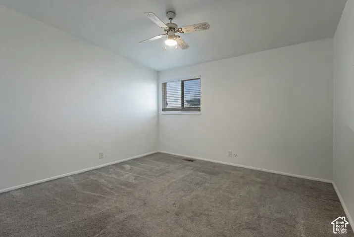 Neutral wall color, carpeted flooring, window with blinds, and a ceiling fan with integrated lighting