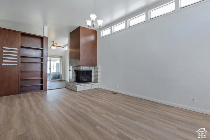 Wood-finish flooring, built-in shelving, white brick fireplace with a wood surround, upper transom windows, and a ceiling-mounted light fixture