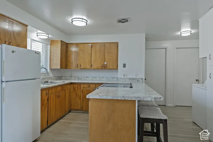 Kitchen featuring wood cabinetry, light-toned laminate countertops, a built-in cooktop, and wood-finish flooring