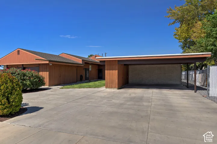 Single-story residence featuring wood panel siding, a carport, concrete driveway, and mature landscaping