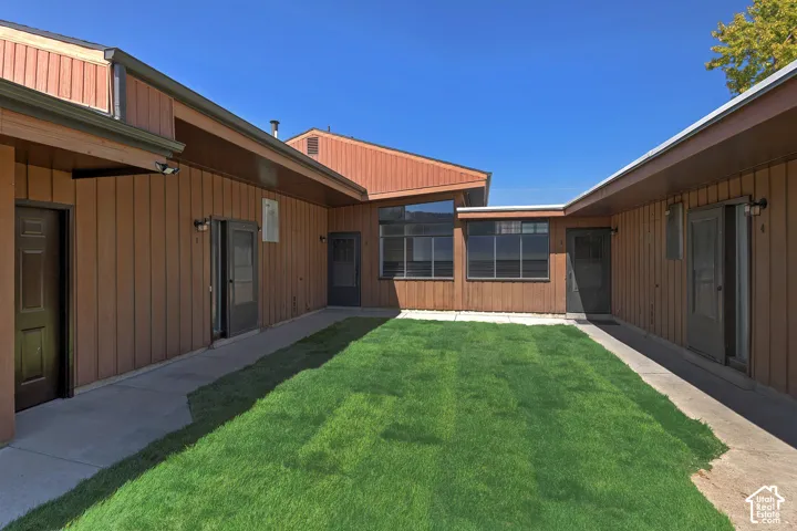 Central courtyard with a manicured lawn, concrete walkways, wood panel siding, and multiple exterior entry doors