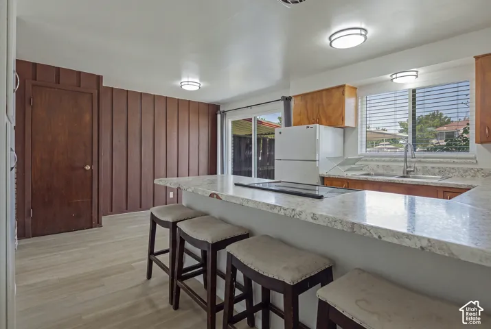 Wood-finish flooring, wood panel accent wall, spacious kitchen island with integrated cooktop, stone-finish countertops, and wood cabinetry
